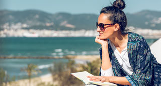 female reading a book in medical detox on balcony with los angeles beach in background